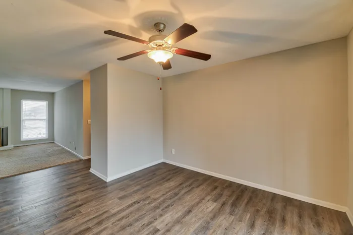 Inviting living space with stylish wooden flooring, ceiling fan, and ample natural light from large window.