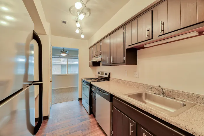 Contemporary kitchen with sleek appliances, elegant dark wood cabinets, and polished countertops, leading into a bright dining area.
