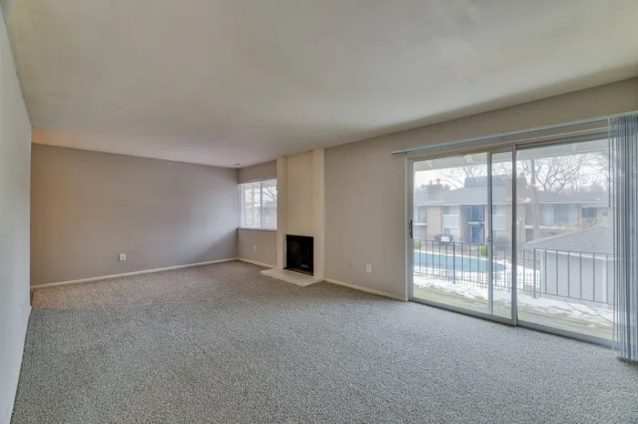 Elegant living room with plush carpet, cozy fireplace, and floor-to-ceiling windows offering scenic balcony views.
