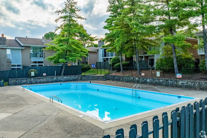 Inviting community pool surrounded by lush greenery and charming residential buildings, perfect for relaxation and leisure.