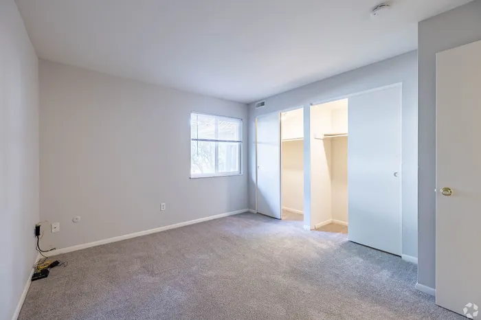 Bright and airy bedroom with plush carpeting, large window for natural light, and spacious dual closets.