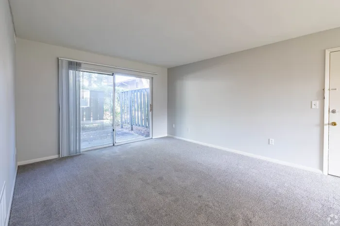 Bright and airy living room with plush carpet, featuring a large sliding glass door opening to a private patio.