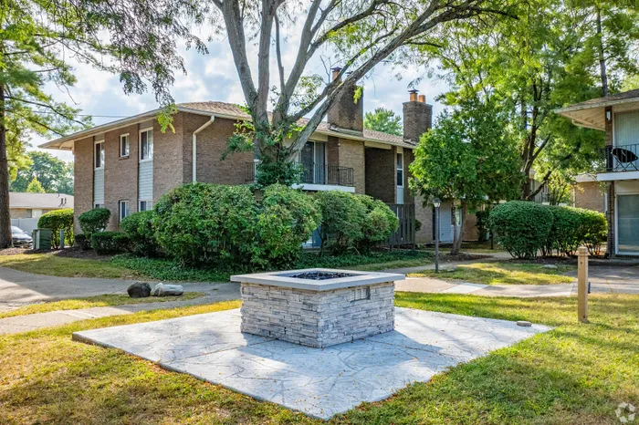 Charming apartment exterior with lush greenery and a cozy outdoor fire pit, perfect for relaxing evenings.