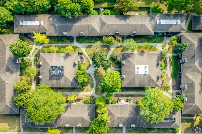Aerial view of a beautifully organized apartment complex surrounded by lush green trees, showcasing well-maintained pathways and inviting communal spaces.