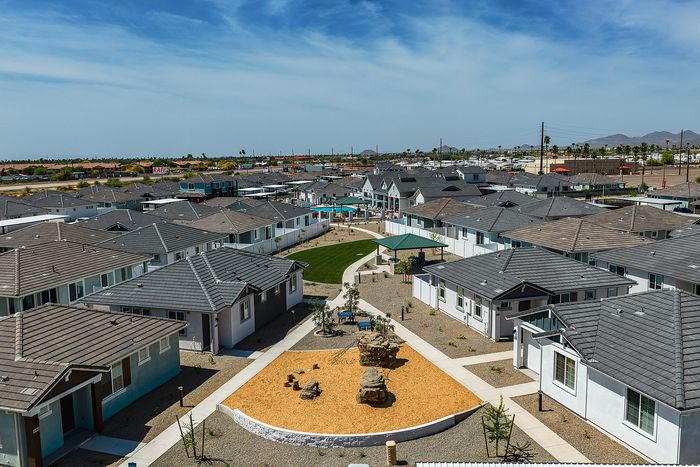 Charming residential community with modern single-story homes, landscaped paths, and inviting green spaces under a vivid blue sky.