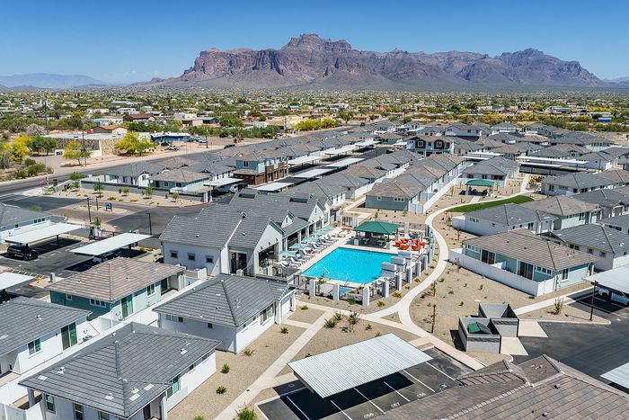 Aerial view of a modern residential community featuring a sparkling blue swimming pool surrounded by sun loungers, with beautiful mountain views in the background.