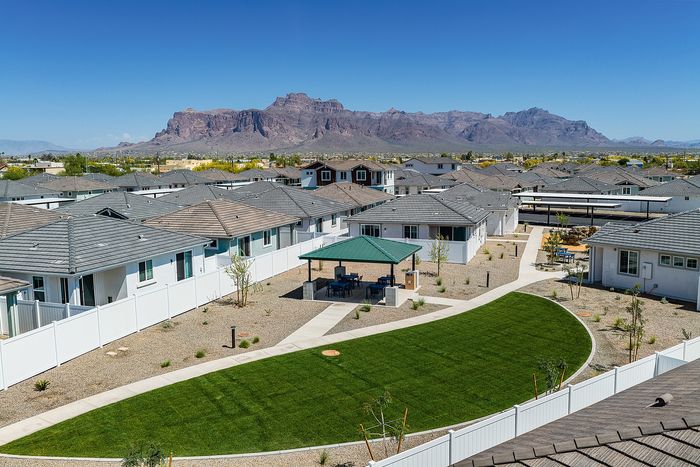 Gorgeous aerial view of a peaceful residential community, showcasing modern homes with pristine white fences and a picturesque mountain backdrop on a clear blue sky day.