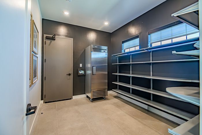 Modern utility room featuring sleek stainless steel refrigerator, ample shelving, and elegant lighting for an organized and stylish space.