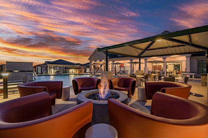 Luxurious outdoor lounge with modern fire pit, surrounded by seating, overlooking a shimmering pool at sunset.