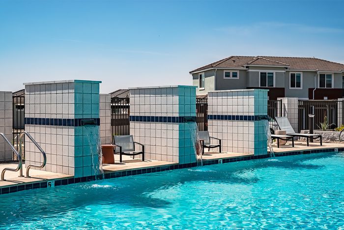 Inviting outdoor pool area with cascading water features, modern lounge chairs, and a peaceful atmosphere under a clear blue sky.