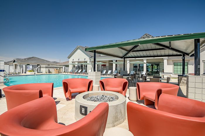 Luxurious outdoor pool area with modern red lounge chairs and a stylish fire pit, perfect for relaxation and socializing.