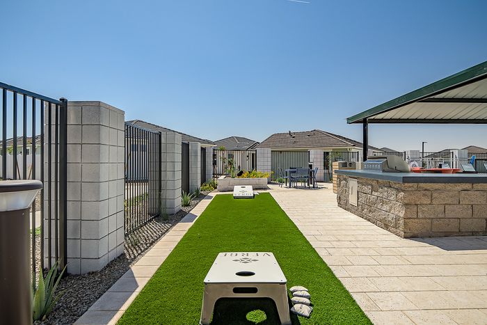 Modern outdoor leisure area featuring a sleek barbecue station, vibrant green turf for games, and inviting dining space under a clear sky.