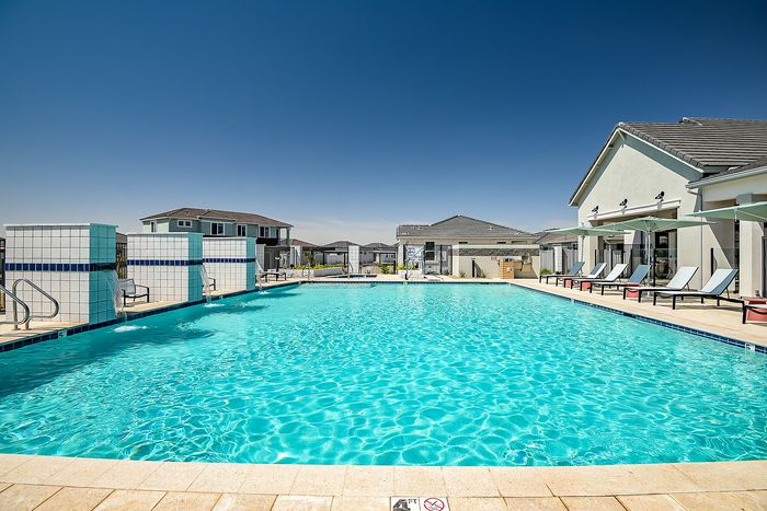 Luxurious outdoor pool area with sun loungers and shaded seating, surrounded by modern architecture under a clear blue sky.