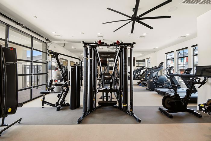 Modern fitness center with state-of-the-art gym equipment, including treadmills, stationary bikes, and strength training machines, in a bright and spacious room with large windows.