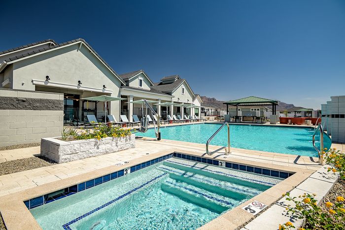 Luxurious apartment complex showcasing a stunning swimming pool and spa under clear blue skies, with elegant lounge chairs and vibrant landscaping.