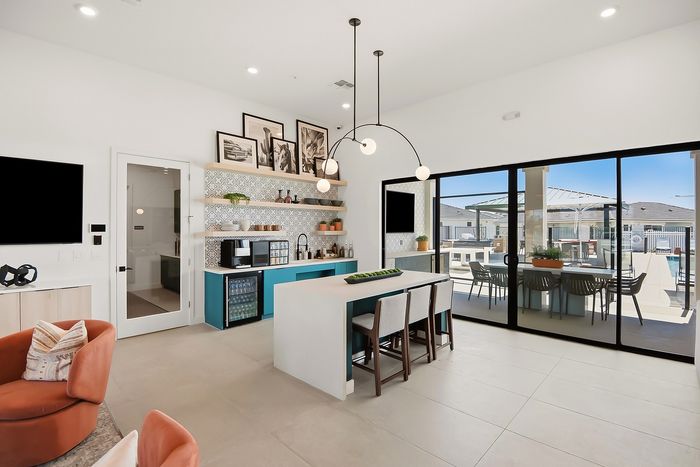 Modern kitchen and dining area with sleek island, artistic decor, and open access to a sunlit patio with outdoor seating.