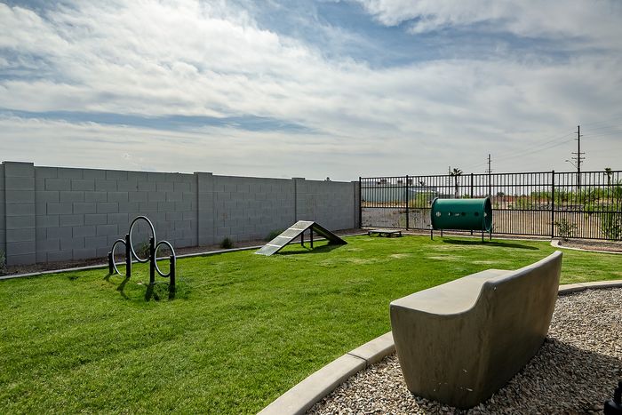 Pet-friendly outdoor area featuring a lush green lawn, agility equipment, and modern seating under a bright sky.
