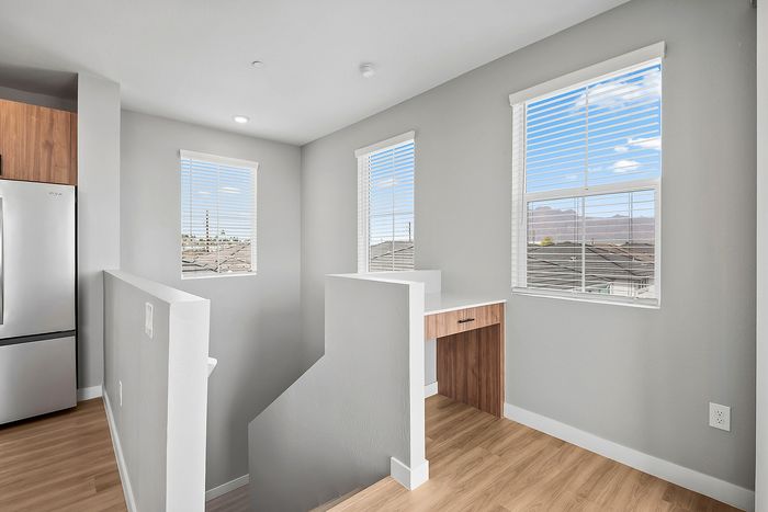 Bright and modern loft area with natural light, featuring sleek wooden flooring and a convenient built-in desk, ideal for a home office setup.