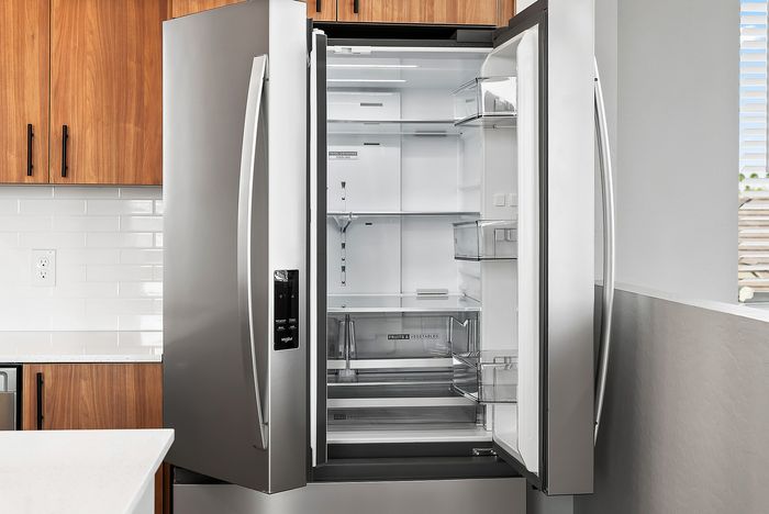 Sleek modern kitchen with a stainless steel French door refrigerator, complemented by elegant wood cabinets and pristine white tile backsplash.
