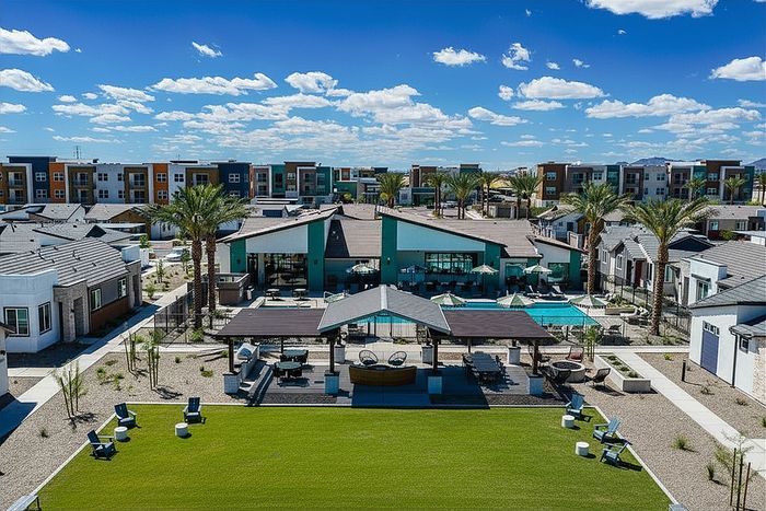 Stunning outdoor view of a modern apartment complex featuring a luxurious pool, vibrant landscaping, and stylish communal seating areas under a clear blue sky.