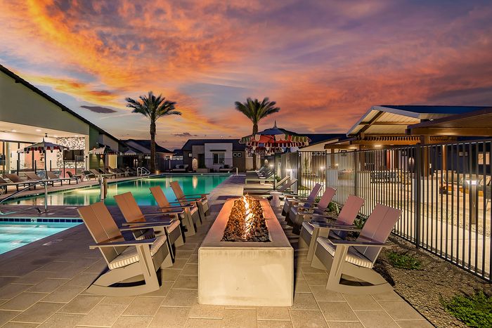 Luxurious outdoor area with a sparkling swimming pool, inviting fire pit, and comfortable seating under a stunning sunset sky.