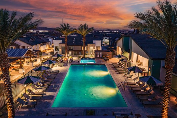 Luxurious apartment complex with a sparkling pool, surrounded by elegant palm trees and vibrant sunset views.