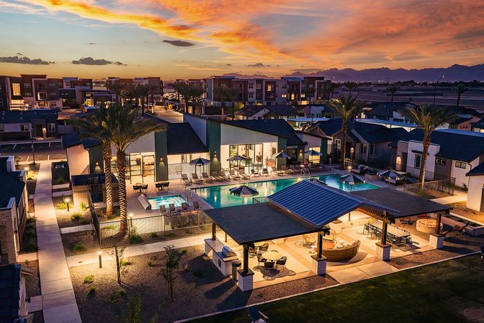 Luxurious apartment complex at sunset featuring a sparkling swimming pool, elegant cabanas, and stunning mountain views.