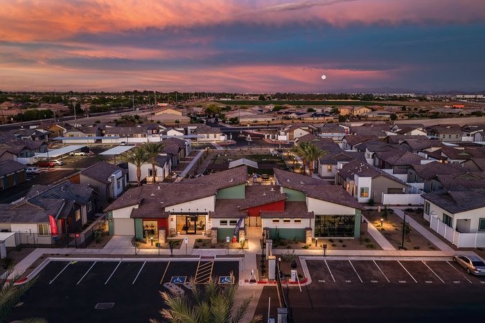 Charming aerial view of a modern housing community at sunset, featuring stylish rooftops, palm trees, and a vibrant sky.