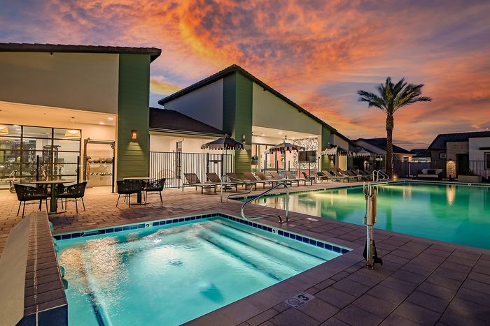 Elegant poolside setting featuring a sparkling swimming pool, cozy loungers, and a vibrant sunset backdrop at a modern apartment complex.