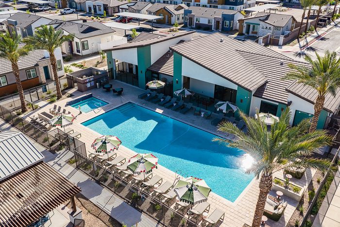 Luxurious apartment complex featuring a stunning outdoor pool area with sun loungers and parasols, surrounded by modern housing and lush palm trees.