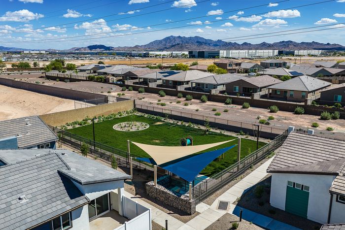Aerial view of a charming neighborhood with picturesque houses, spacious yards, and scenic mountain backdrop under a vibrant blue sky.