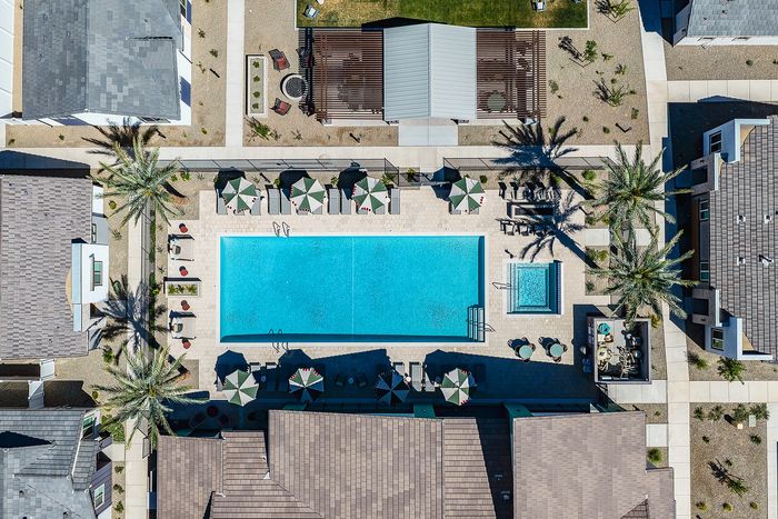 Aerial view of a luxurious apartment complex featuring a sparkling swimming pool, shaded lounge chairs, and surrounding palm trees, offering an upscale resort-style experience.
