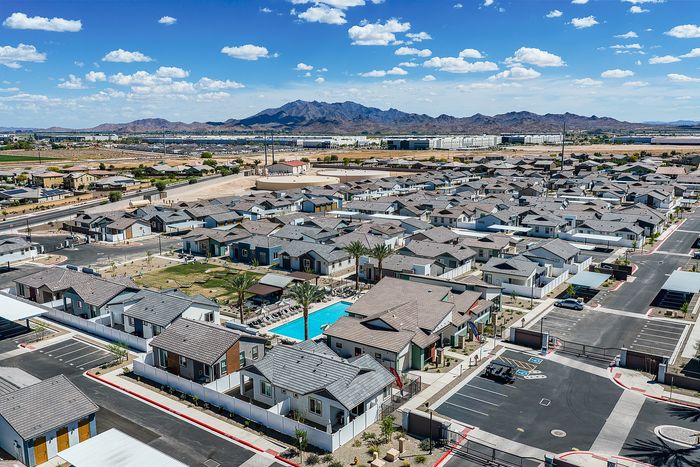 Aerial view of a modern residential community featuring neatly arranged houses with a central swimming pool, set against a stunning mountain backdrop.