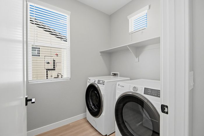 Bright and modern laundry room featuring a sleek washer and dryer set beneath a sunlit window, ideal for efficient living.