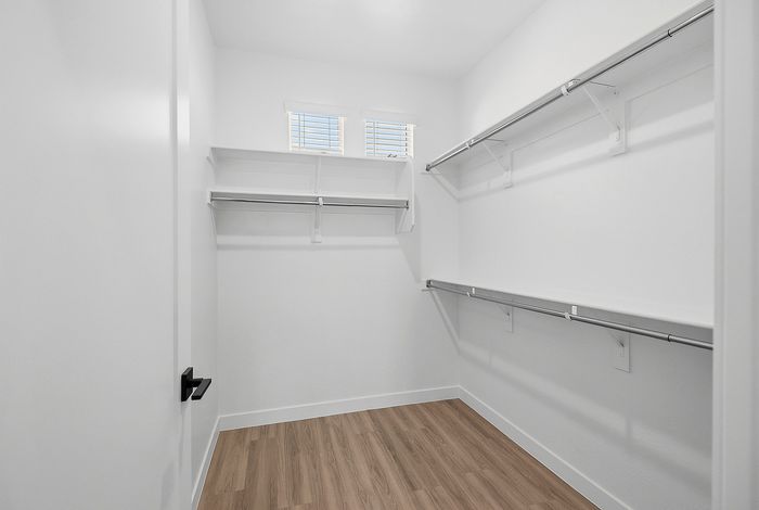Spacious and bright walk-in closet featuring elegant wooden flooring, ample shelving, and sleek chrome clothing rods.
