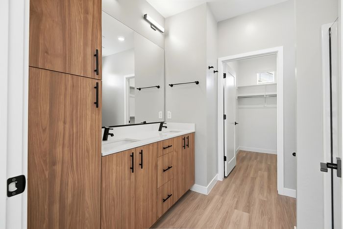 Modern bathroom with sleek double vanity, warm wood cabinets, and a spacious walk-in closet.