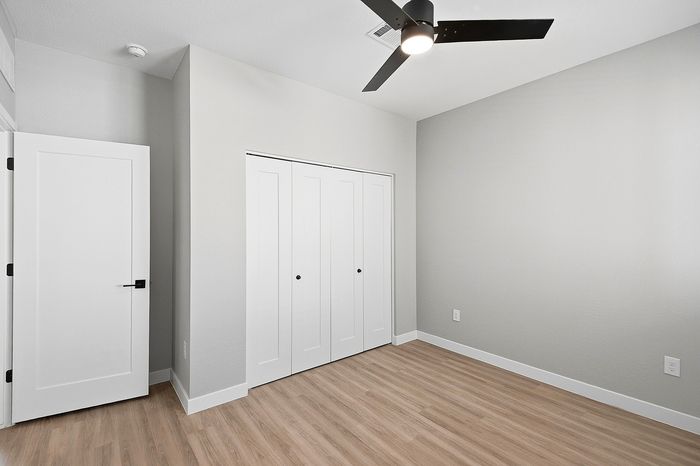 Bright and airy room with sleek wood flooring, spacious closets, and a modern ceiling fan, perfect for a stylish living space.