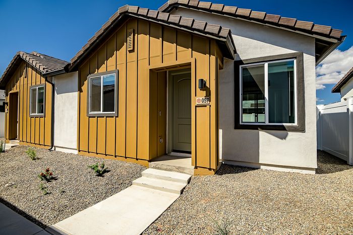 Charming modern home with a stylish mustard and white exterior, featuring sleek windows and inviting entryway under a clear blue sky.