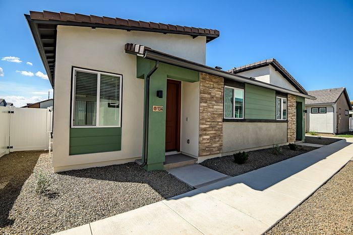 Charming modern home with a mix of stone and siding exterior, featuring a welcoming front entrance and tidy landscaping under a clear blue sky.
