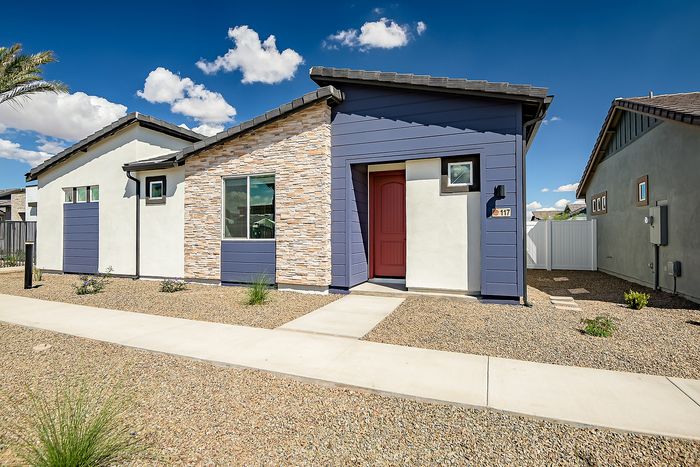 Modern single-story home with elegant stone facade, vibrant red door, and blue accents, set against a bright blue sky.