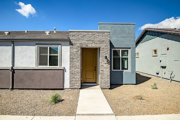 Charming modern home exterior with a stylish brick facade, bright yellow door, and sleek windows under a clear blue sky.