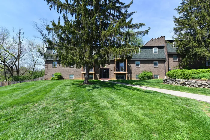 Charming brick apartment building with lush green lawn and mature trees, offering serene living surrounded by nature.