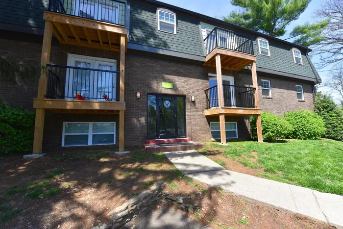 Charming brick apartment building with inviting balconies, lush greenery, and a welcoming entrance.