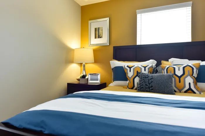 Bright and cozy bedroom with modern decor, featuring a stylish bed adorned with geometric-patterned pillows, a sleek nightstand, and a warm lamp casting a soft glow. Perfect for comfort and relaxation.