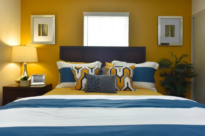 Bright and inviting bedroom with a stylish color palette of mustard and navy, featuring plush pillows, modern decor, and warm ambient lighting.