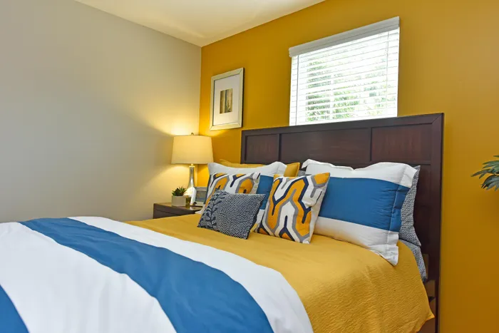 Inviting bedroom with stylish yellow accent wall, plush pillows, and modern decor creating a warm, comfortable atmosphere.