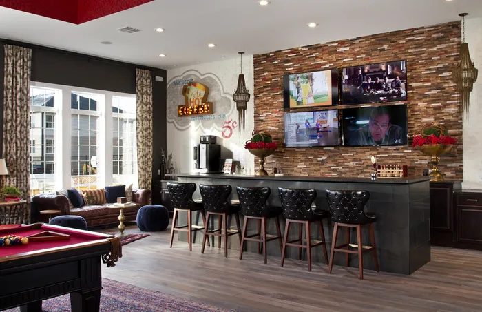 Chic apartment lounge featuring a stylish bar with leather seating, multiple TVs, and a cozy seating area with plush sofas and modern decor.