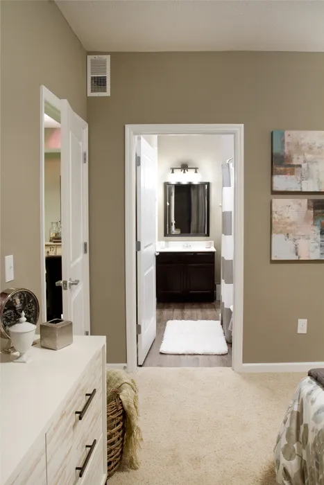 Cozy bedroom with plush carpeting leading to a stylish bathroom, featuring elegant lighting and modern decor.