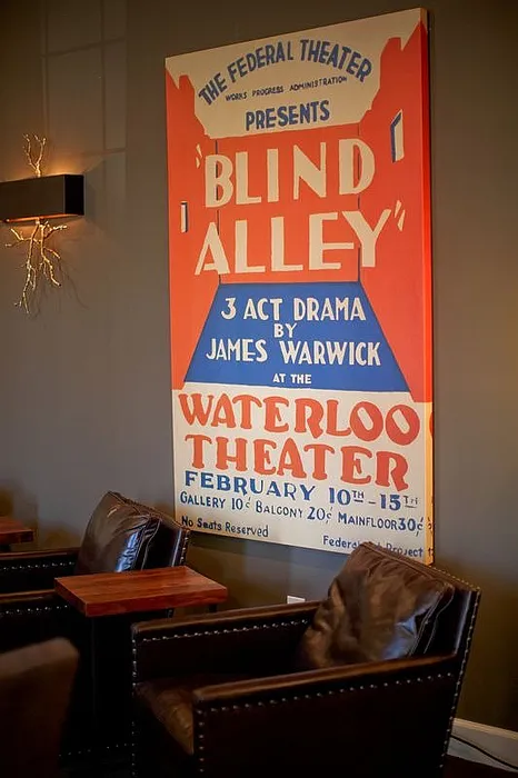 Cozy theater lounge with vintage poster of 'Blind Alley' at Waterloo Theater, featuring plush leather chairs and elegant decor.