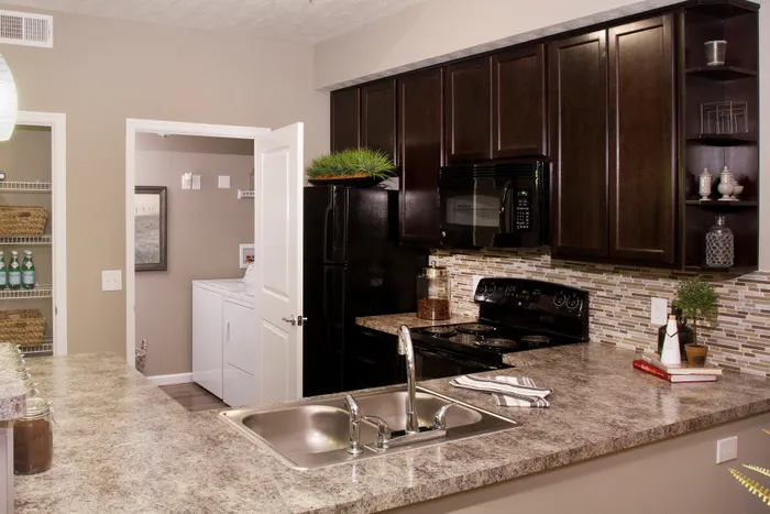Elegant modern kitchen with dark wood cabinets, granite countertops, and sleek appliances, leading to a cozy laundry room.